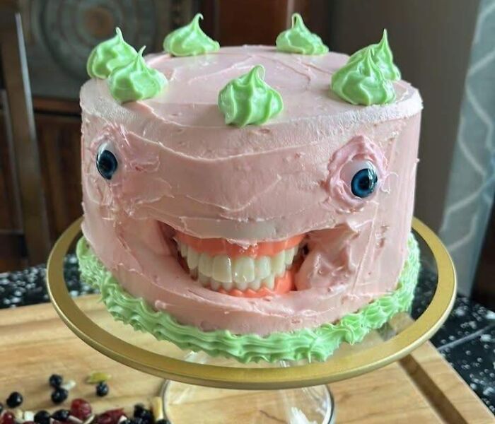 Pink cake with green frosting and a set of false teeth creating a bizarre and horrible craft appearing like a face.