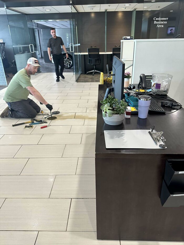 Worker kneeling on office floor attempting repairs while another man watches, an example of epic work fails in a business setting.