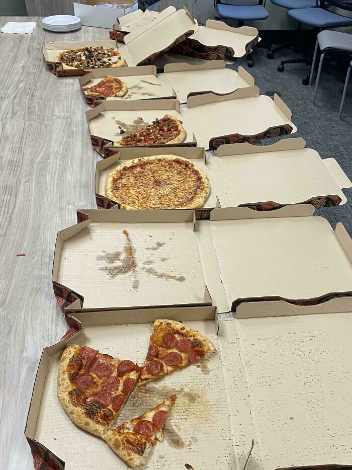Partially eaten pizzas in open boxes lined up on a table, showcasing an epic work fail with leftover food.