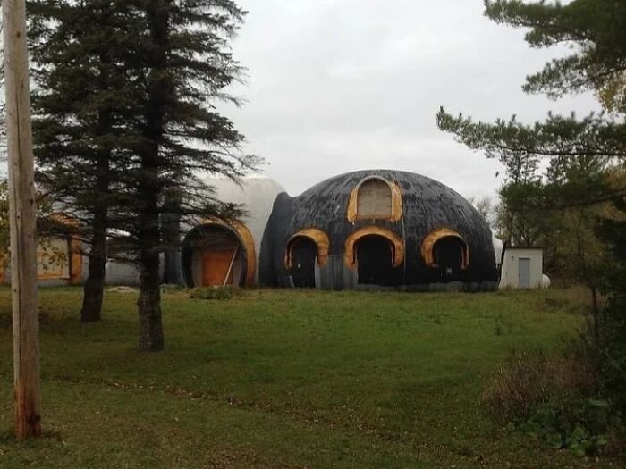 Unhinged real estate listing showing an unusual dome-shaped house with arched wooden doorways in a grassy area.