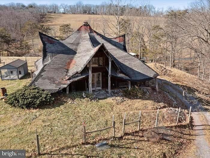 Unhinged real estate listing showing a bizarre, worn house with a warped roof in a rural, barren landscape.