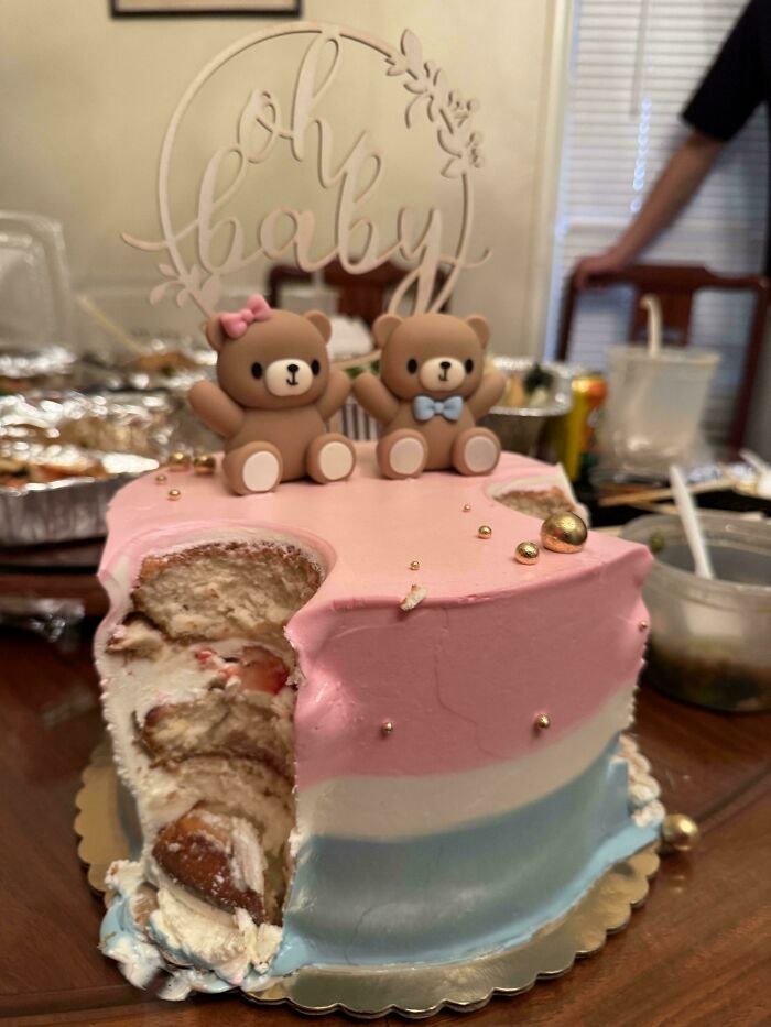 Partially eaten pink, white, and blue baby shower cake with two teddy bear toppers, illustrating funny unfortunate situations.