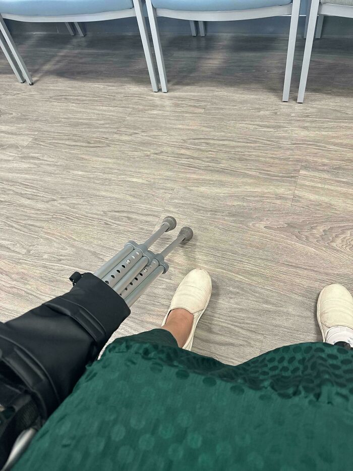 Person wearing white slip-on shoes and green skirt, holding crutches in a waiting room, highlighting funny unfortunate situations.