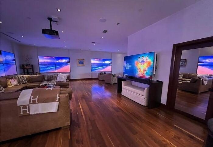 Spacious living room with multiple TVs, modern furniture, and hardwood floors in unhinged real estate listing.