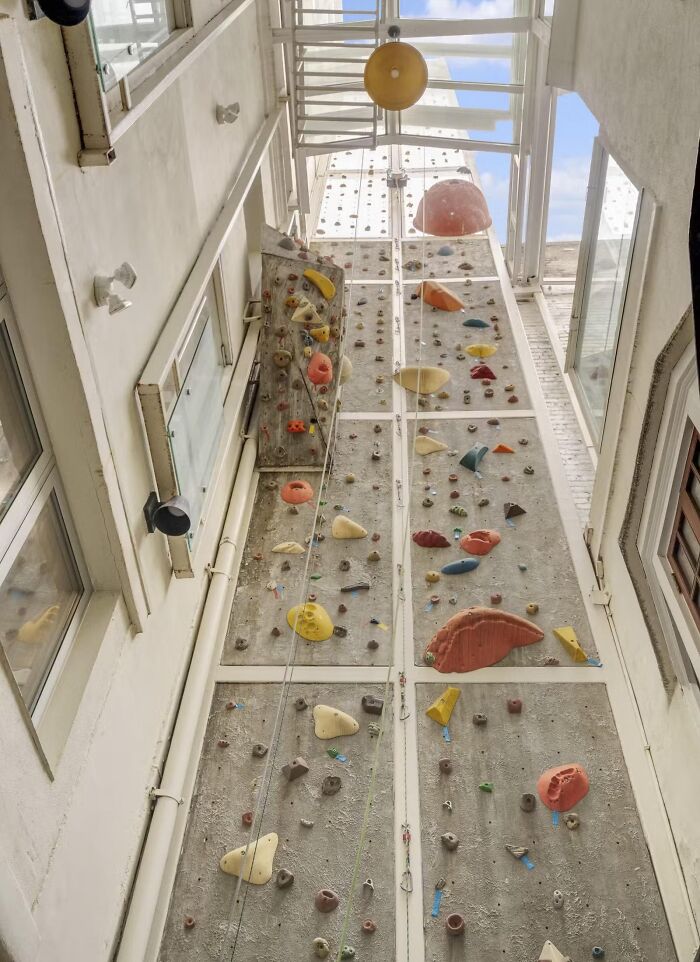 Indoor rock climbing wall inside a narrow real estate space with bright colored holds and skylight above.