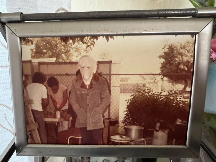 Old photo of a mysterious elderly person standing with hands in pockets in a vintage outdoor setting, intriguing mystery concept.