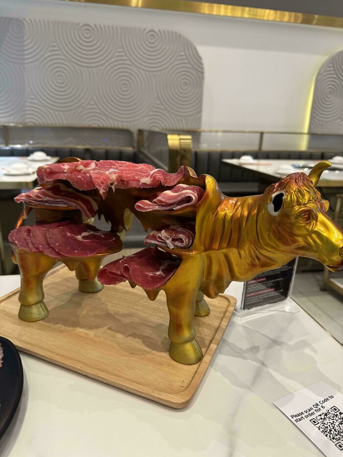 Golden cow-shaped charcuterie holder serving thinly sliced meat in an unexpected and unholy meal presentation.