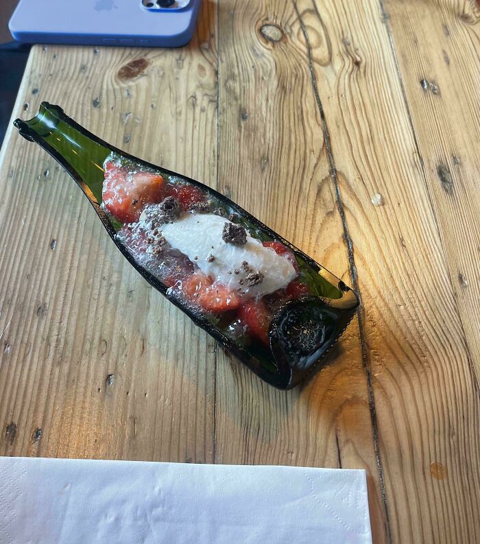 Meal served in a creatively cut glass bottle on a wooden table, showcasing unholy and unexpected food presentation.