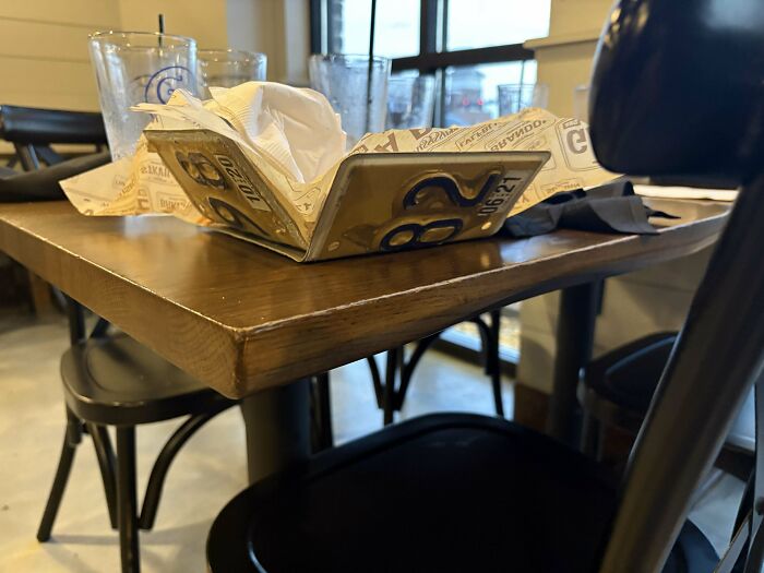 Unholy meal serving using a folded pizza box as a tray with empty glasses on a wooden restaurant table.