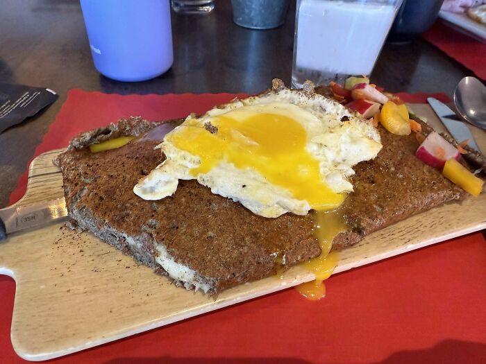 Meal served with a fried egg and melted yolk on an irregularly shaped, rough-textured dish on a wooden board.