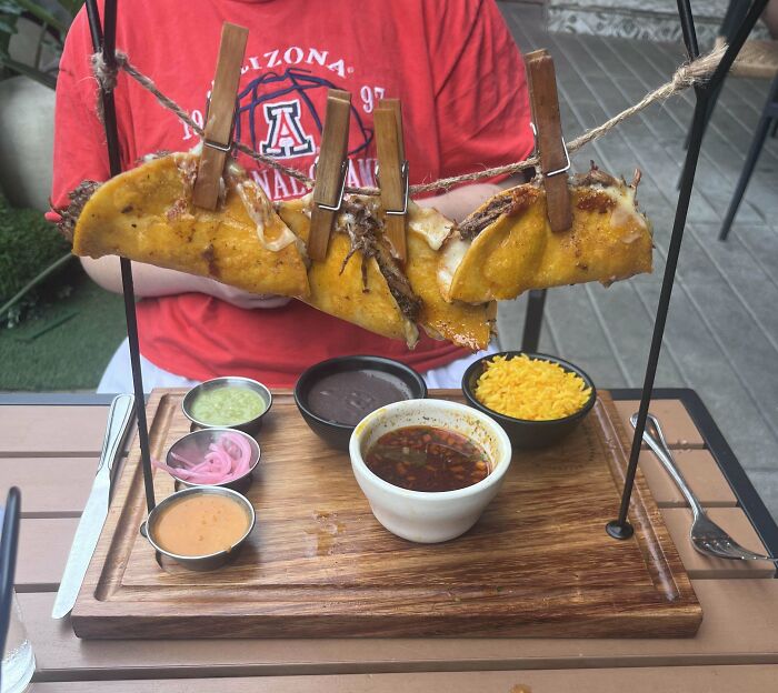Tacos hanging by clothespins on a string above a wooden board with sauces and sides served in an unusual way
