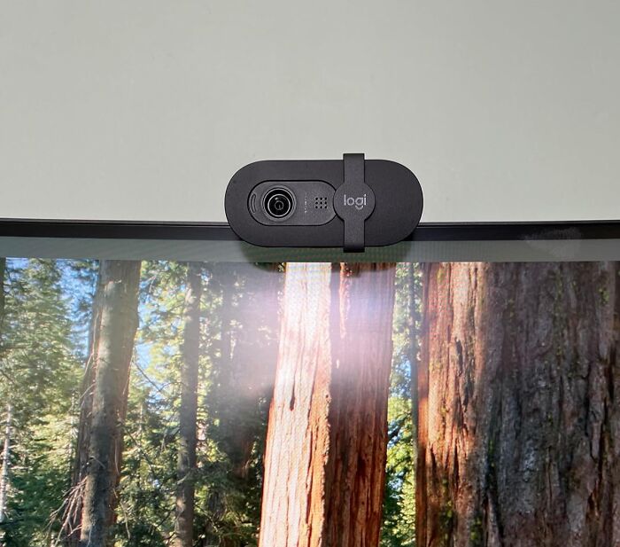 Black Logitech webcam mounted on top of a monitor displaying a forest scene for back-to-school deals.