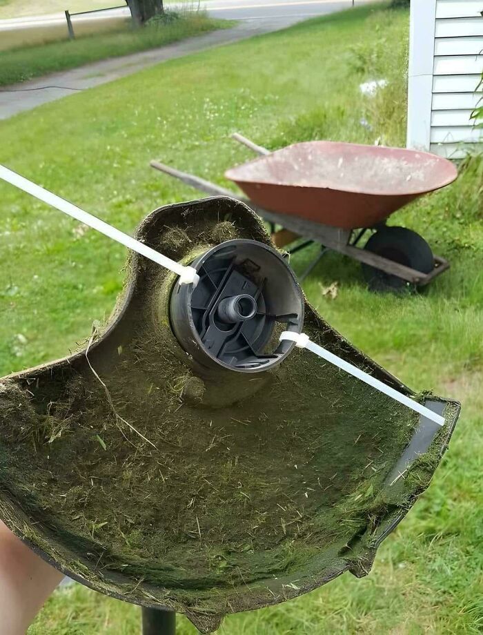 Lawn mower spool fixed with zip ties showing creative redneck engineering repair in a grassy backyard setting.