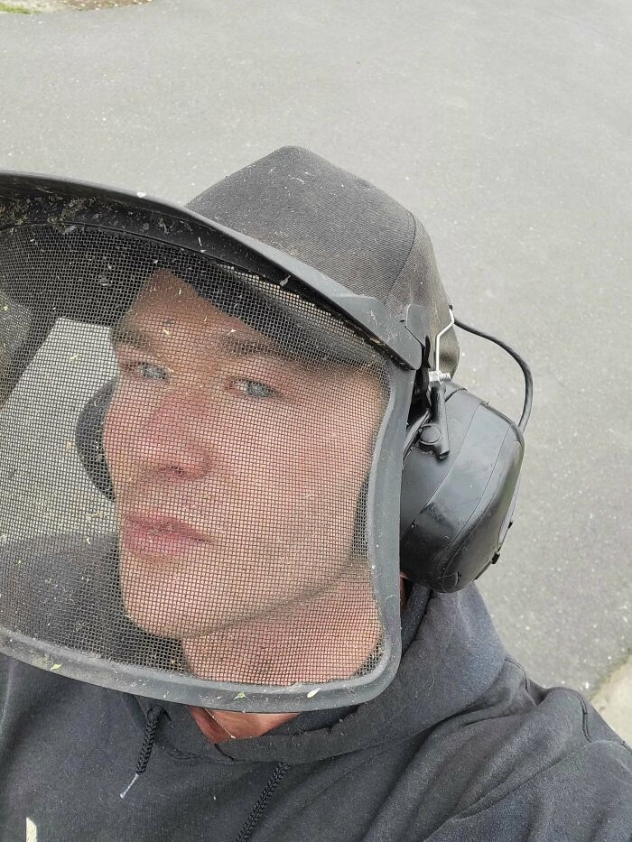 Man wearing DIY protective mesh face shield and headphones, showcasing redneck engineering creativity in outdoor setting