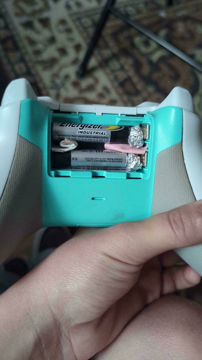 Batteries in a game controller held in hand, showing redneck engineering fix with foil and tape for better contact.