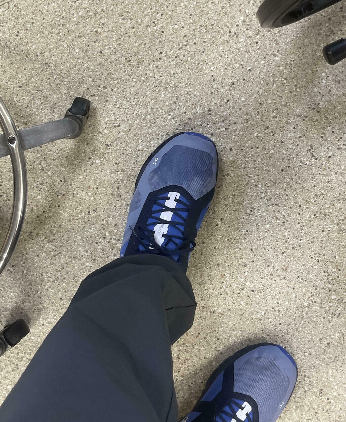 Close-up of work shoes with a broken wheelchair wheel nearby, showing an epic work fail on a speckled floor.