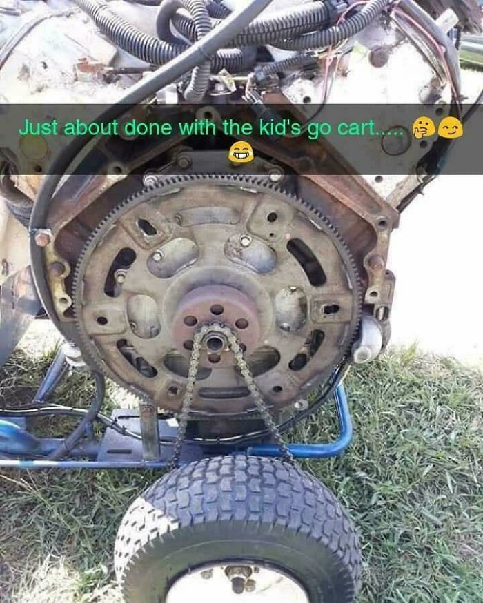 Close-up of redneck engineering go-kart engine with improvised chain drive connected to a small tire on grass.