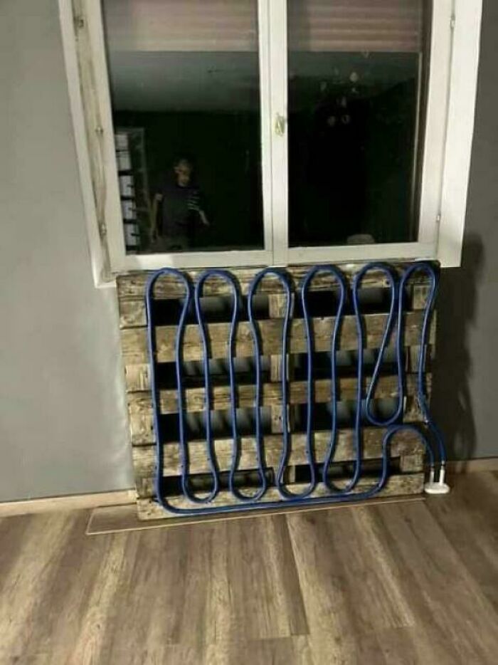 Improvised redneck engineering heating system made from a wooden pallet and coiled blue tubing under a window.