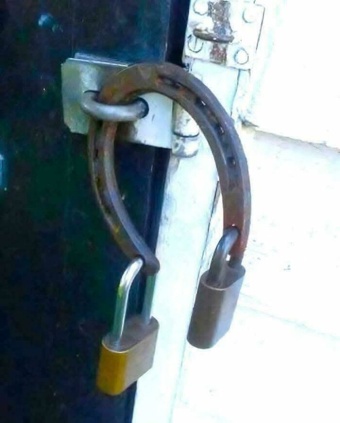 Rusty horseshoe used as a lock holder securing two padlocks on a door latch, an example of redneck engineering.
