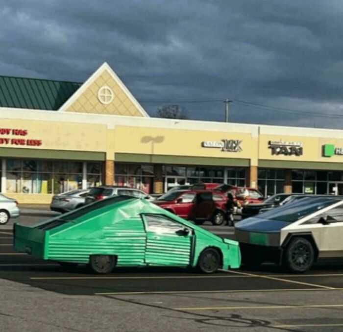 Green homemade car resembling a retro style parked next to a modern vehicle in a shopping center lot showing redneck engineering.