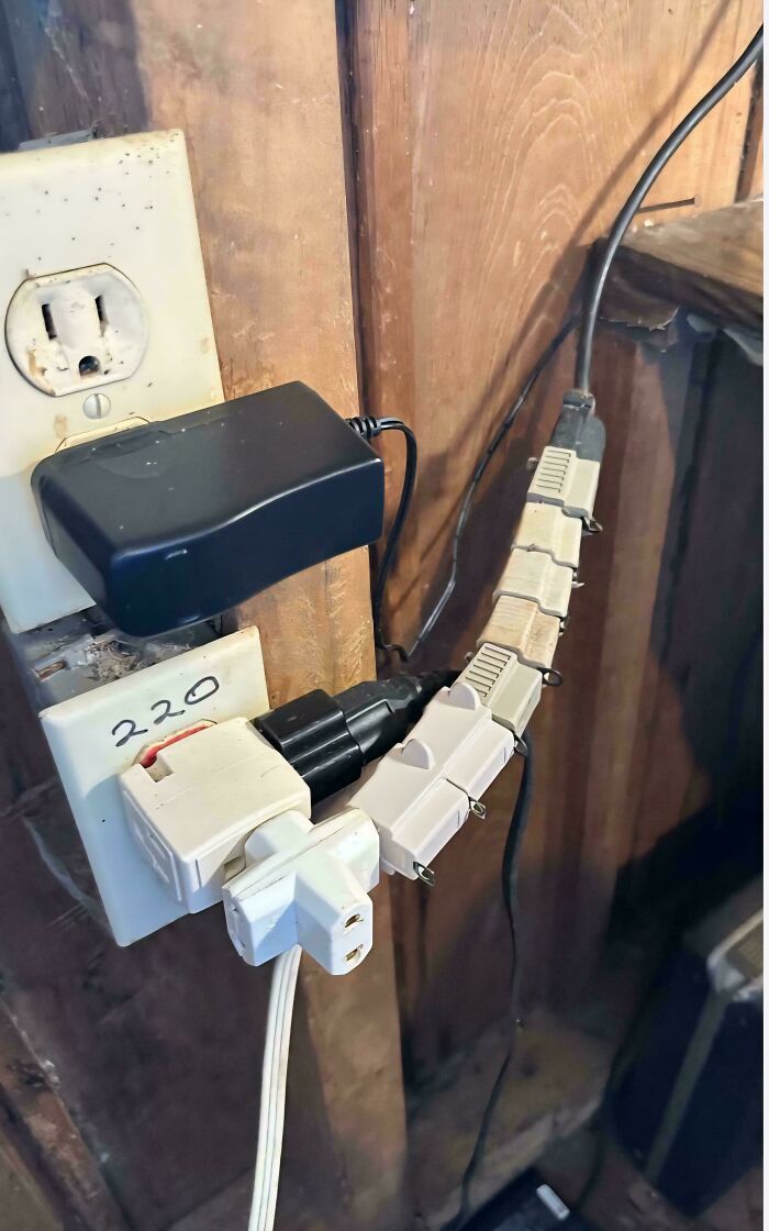 Improvised redneck engineering power strip made from multiple adapters connected on a wooden wall outlet.