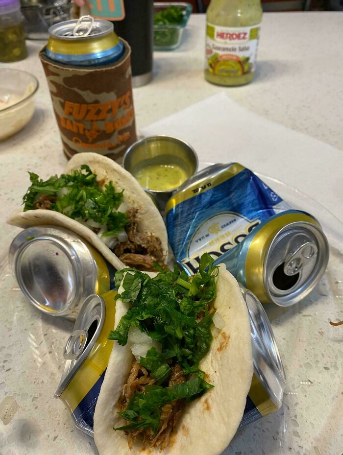 Tacos held upright by crushed beer cans on a plate with sauce, showcasing redneck engineering creativity.