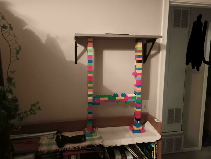 Creative redneck engineering using colorful building blocks to support a shelf in a home setting with tools nearby.
