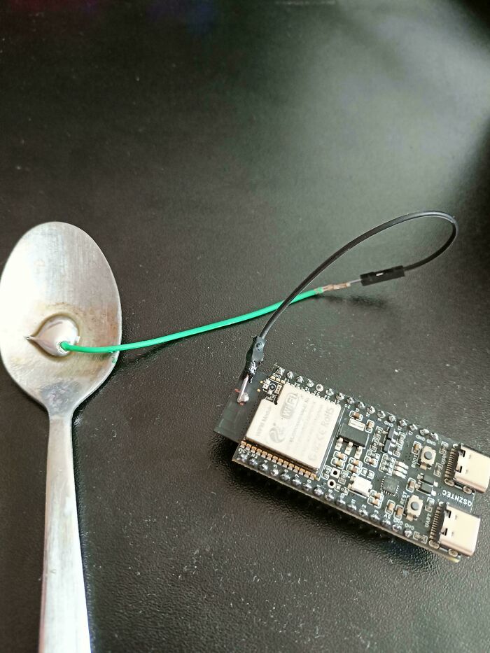 Electronic circuit board connected to a spoon with wires, showcasing redneck engineering and creative MacGyvering.