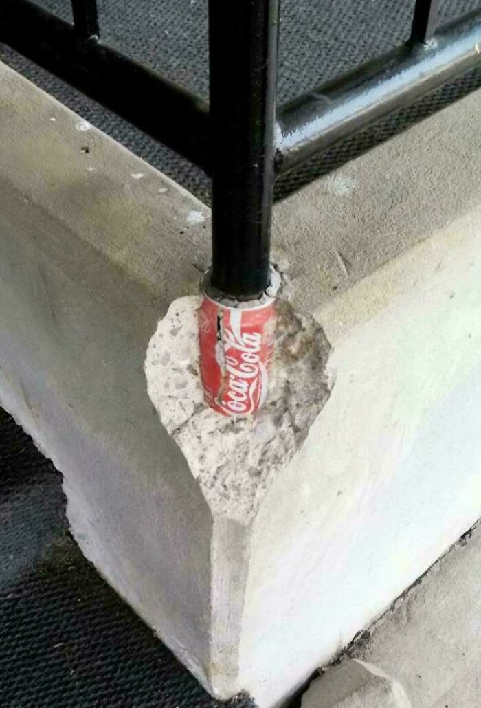 Metal railing supported by a crushed soda can embedded in concrete showing redneck engineering creativity.