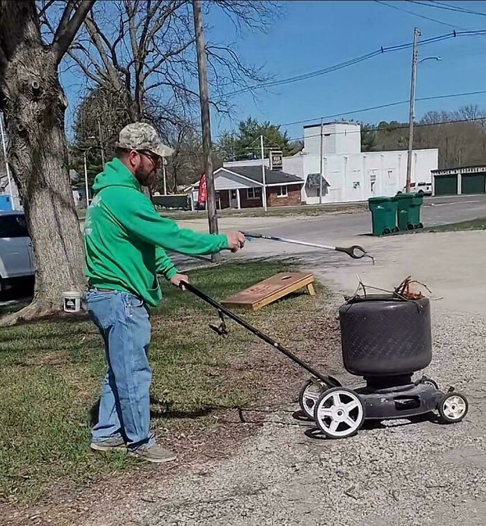Man using redneck engineering to turn a lawnmower into a portable fire pit outside on a sunny day.