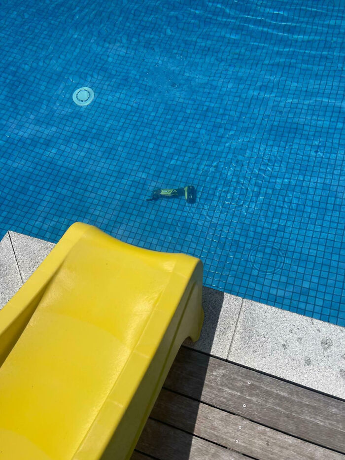 Yellow slide by pool with a power drill accidentally dropped into the water, an epic work fail moment outdoors.