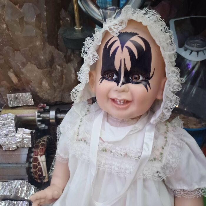 Porcelain doll with creative face paint in a lace bonnet and dress showcasing redneck engineering creativity.