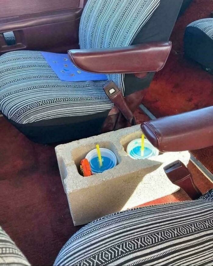 Car interior showing creative redneck engineering with a cinder block used as a cup holder between seats.
