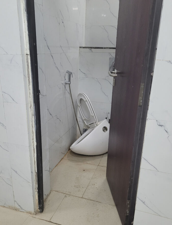 Broken toilet bowl detached on the floor in a small bathroom, showing an epic work fail in a tiled restroom.