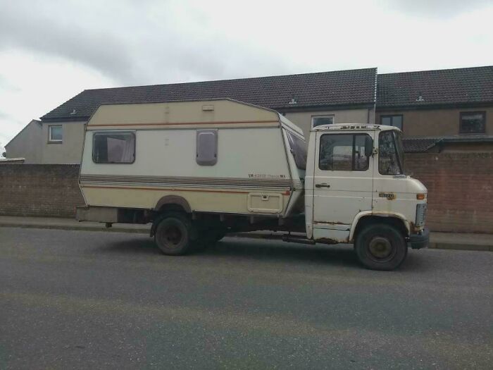 Old truck with a camper creatively attached showcasing redneck engineering and inventive MacGyvering on a residential street.