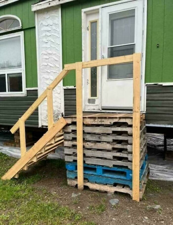Improvised wooden staircase made from pallets and planks providing access to a raised doorway in redneck engineering style.