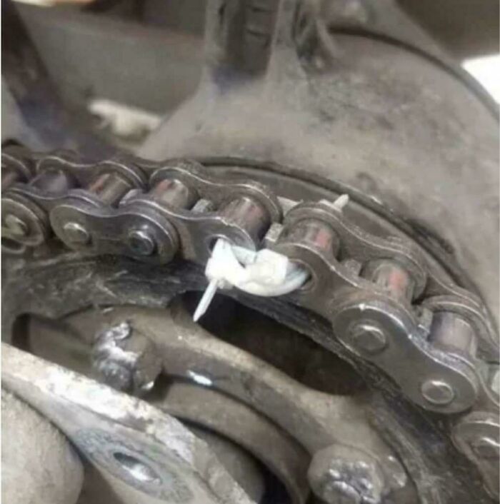 Close-up of a motorcycle chain repaired using makeshift redneck engineering with zip ties as a temporary fix.