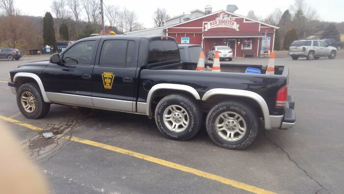 Modified black pickup truck with six wheels parked outside a restaurant, showcasing redneck engineering creativity.