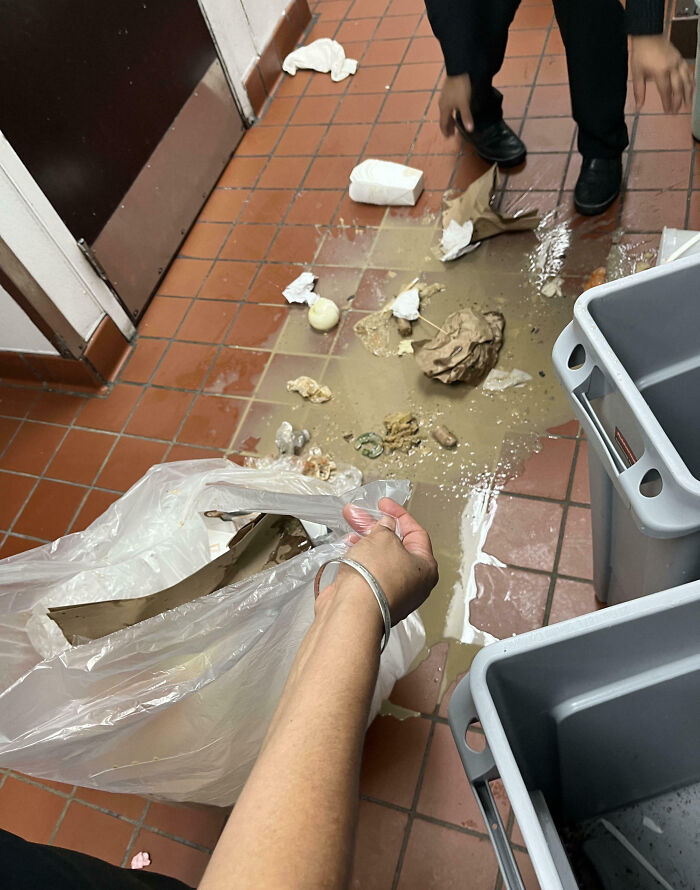 Person cleaning up spilled trash and liquid on the floor in a workplace, showing an epic work fail scene.