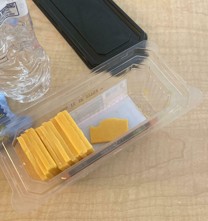 Plastic cheese container with neatly stacked slices and one broken slice beside them on a wooden desk, an epic work fail.