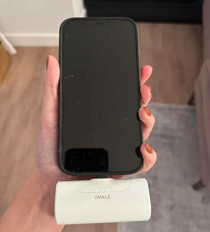 Hand holding smartphone connected to portable charger showing travel essentials for hot girl summer itinerary.