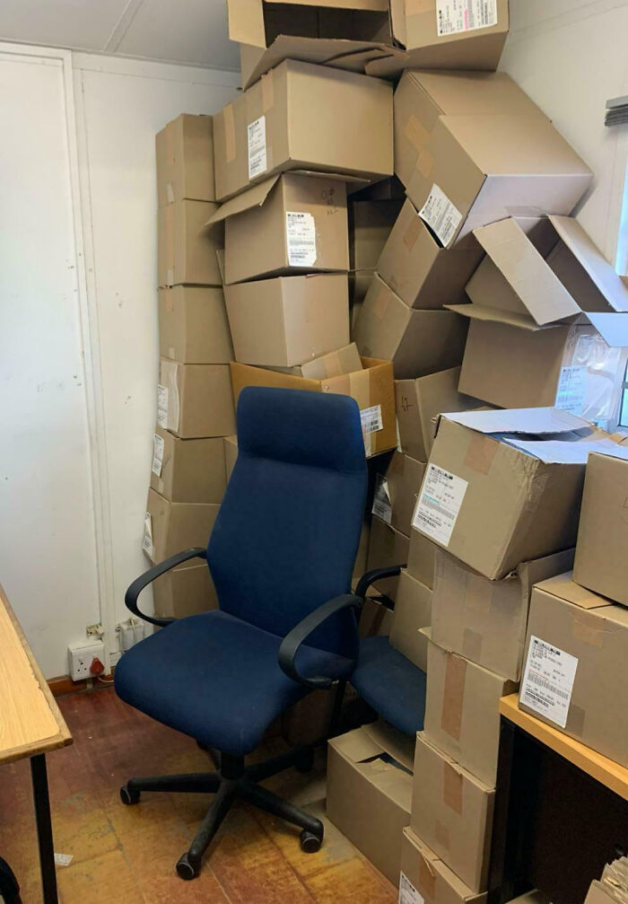 Office chair surrounded and nearly buried by a large stack of cardboard boxes showing epic work fails.