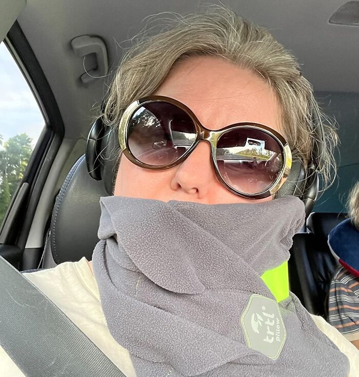 Woman wearing oversized sunglasses and a travel pillow in a car, showing travel essentials for hot girl summer itinerary.