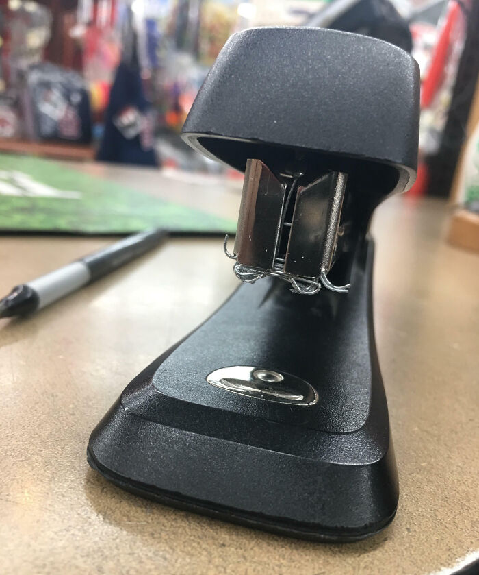 Black stapler with bent staples stuck inside, illustrating an epic work fail on an office desk surface with a marker nearby.