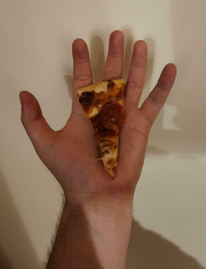 Hand holding a small slice of pepperoni pizza, illustrating an epic work fail involving portion size.
