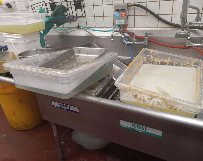 Dirty food trays left unwashed in a commercial kitchen sink showing an epic work fail causing hygiene issues.