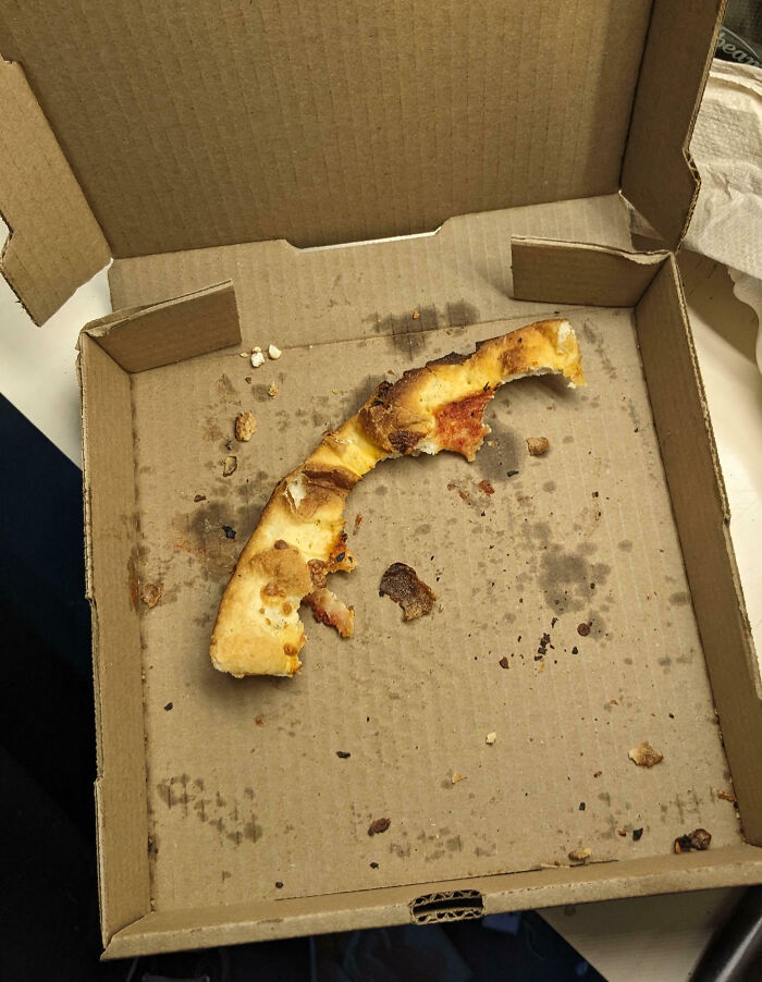 Half-eaten pizza crust left in a greasy cardboard box showing an epic work fail moment at the office.