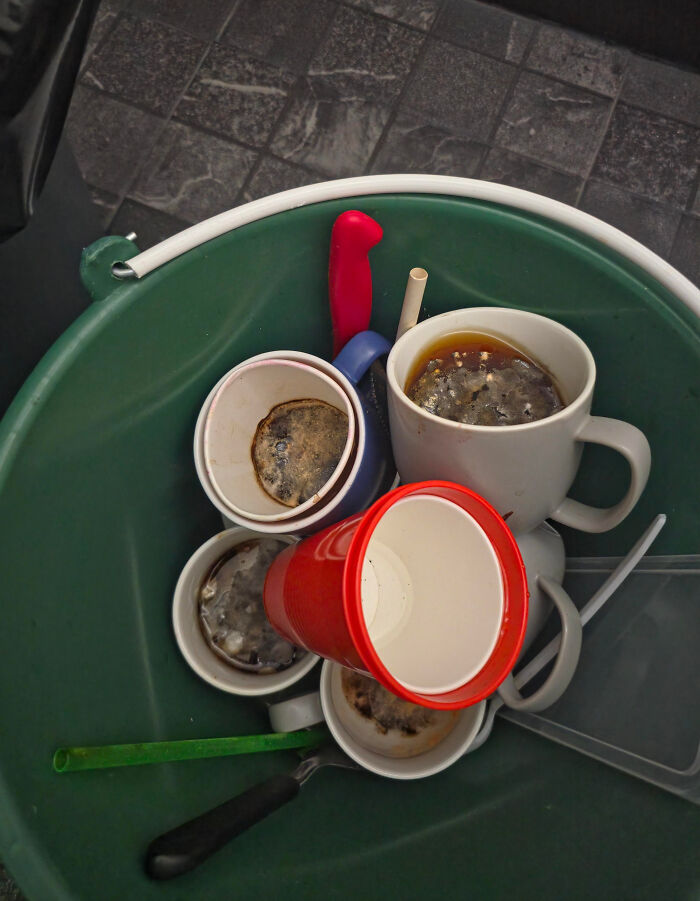 Green trash bin filled with dirty coffee mugs and cups, illustrating an epic work fail scene.