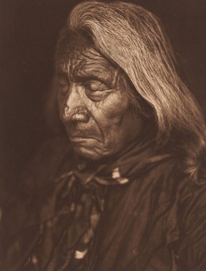 Sepia portrait of an elderly Native American man with long hair, featured in Edward S. Curtis photos preserving history.