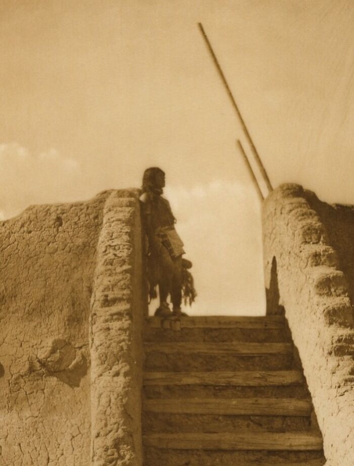 Native American figure standing on adobe steps in a vintage sepia Edward S. Curtis photo preserving history.